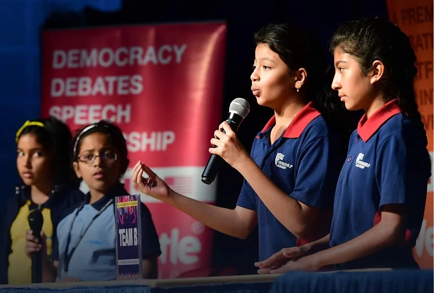 Students in uniform holding a microphone during a live Debate Battles session, mastering persuasion and public speaking skills