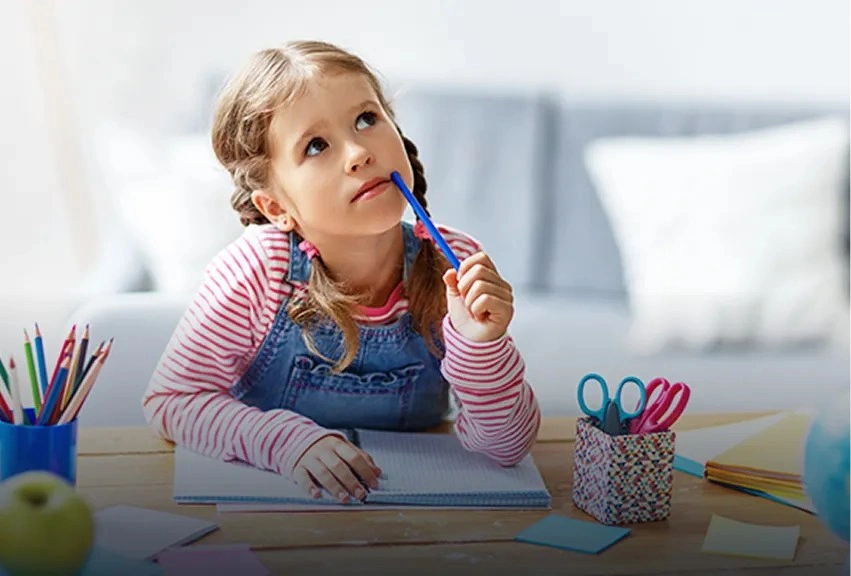 Young girl thinking creatively while writing at a desk with colored pencils, developing storytelling and self-expression skills